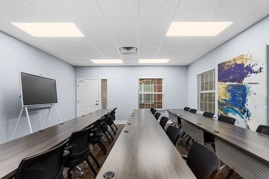 Conference room in classroom-style layout with parallel rows of tables, seating, and a presentation display at ProSpace Gainesville