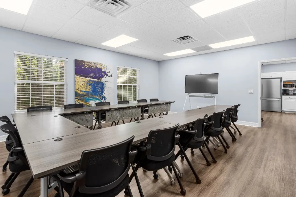 Conference room in a U-shaped table arrangement with a large display; adjoining kitchen area visible in the background at ProSpace Gainesville